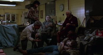 Movie still from “The Return of the Living Dead” (1985), directed by Dan O'Bannon – A group of people sitting and standing in a room; Wide shot, High angle