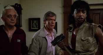 Movie still from “The Return of the Living Dead” (1985), directed by Dan O'Bannon – A man holding a gun while standing next to another man; Medium shot, Low angle