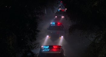 Movie still from “The Return of the Living Dead” (1985), directed by Dan O'Bannon – A line of police cars driving down a street at night; Extreme Wide shot, High angle