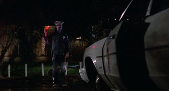 Movie still from “The Return of the Living Dead” (1985), directed by Dan O'Bannon – A police officer standing in front of a wrecked car at night; Wide shot, Low angle