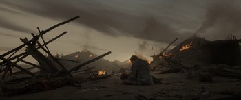 Movie still from “The Revenant” (2015), directed by Alejandro G. Iñárritu – A man sitting on the ground in front of a fire pit; Wide shot, Low angle