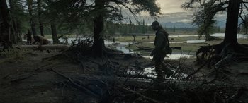 Movie still from “The Revenant” (2015), directed by Alejandro G. Iñárritu – A man walking across a river near a tree; Wide shot, Over the shoulder angle