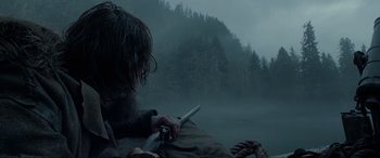 Movie still from “The Revenant” (2015), directed by Alejandro G. Iñárritu – A man holding a knife in his hand while sitting on a boat; Medium shot, Low angle