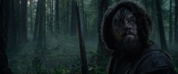 Movie still from “The Revenant” (2015), directed by Alejandro G. Iñárritu – A man with a rifle in a forest; Close Up shot, Low angle