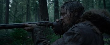 Movie still from “The Revenant” (2015), directed by Alejandro G. Iñárritu – A man with a gun in the woods with trees in the background; Close Up shot, Low angle
