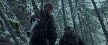 Movie still from “The Revenant” (2015), directed by Alejandro G. Iñárritu – Two men are standing in the woods holding guns; Medium shot, Low angle