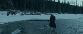 Movie still from “The Revenant” (2015), directed by Alejandro G. Iñárritu – A man in a long coat walking across a river; Wide shot, High angle