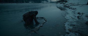 Movie still from “The Revenant” (2015), directed by Alejandro G. Iñárritu – A person in a body of water surrounded by rocks; Wide shot, High angle