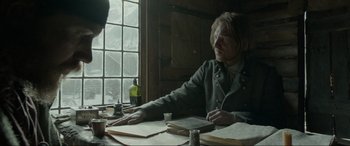 Movie still from “The Revenant” (2015), directed by Alejandro G. Iñárritu – A man sitting at a table writing on a piece of paper; Medium shot, Over the shoulder angle