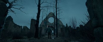 Movie still from “The Revenant” (2015), directed by Alejandro G. Iñárritu – A person standing in front of a building in the dark; Extreme Wide shot, Low angle