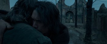 Movie still from “The Revenant” (2015), directed by Alejandro G. Iñárritu – A man with long black hair is leaning against a building; Close Up shot, Low angle
