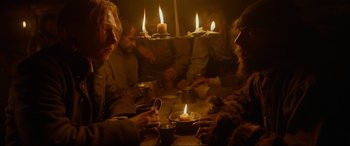 Movie still from “The Revenant” (2015), directed by Alejandro G. Iñárritu – A group of people sitting around a table with candles on it; Medium shot, Low angle