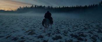 Movie still from “The Revenant” (2015), directed by Alejandro G. Iñárritu – A person riding a horse in a snowy field at night; Extreme Wide shot, High angle