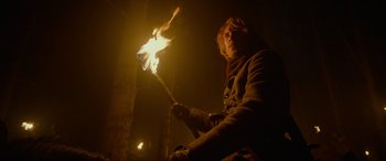 Movie still from “The Revenant” (2015), directed by Alejandro G. Iñárritu – A person holding a stick with a flame in it; Medium shot, Low angle