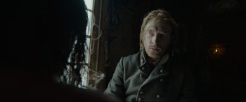 Movie still from “The Revenant” (2015), directed by Alejandro G. Iñárritu – A man with blonde long hair sitting in front of a window; Close Up shot, Over the shoulder angle