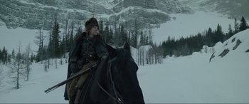 Movie still from “The Revenant” (2015), directed by Alejandro G. Iñárritu – A man riding on the back of a black horse in the snow; Wide shot, Low angle