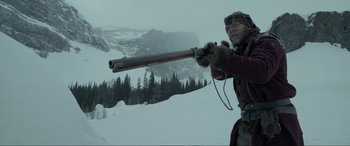 Movie still from “The Revenant” (2015), directed by Alejandro G. Iñárritu – A man holding a rifle on top of a snow covered slope; Medium shot, Over the shoulder angle
