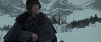 Movie still from “The Revenant” (2015), directed by Alejandro G. Iñárritu – A man wearing a fur hat and a coat in the middle of a snow covered mountain; Medium shot, Low angle