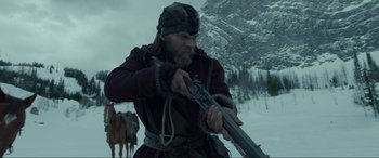 Movie still from “The Revenant” (2015), directed by Alejandro G. Iñárritu – A man holding a rifle while standing in the snow; Medium shot, Low angle