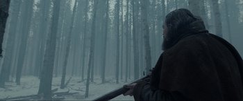 Movie still from “The Revenant” (2015), directed by Alejandro G. Iñárritu – A man with a beard holding a rifle in a snowy forest; Medium shot, Low angle