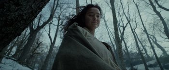 Movie still from “The Revenant” (2015), directed by Alejandro G. Iñárritu – A woman wrapped in a blanket standing in the woods; Close Up shot, Low angle