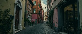 Movie still from “The Ritual Killer” (2023), directed by George Gallo – An alley way in a european city with buildings and plants; Extreme Wide shot, Low angle