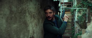 Movie still from “The Ritual Killer” (2023), directed by George Gallo – A man holding a gun while standing next to a wall; Medium shot, Low angle