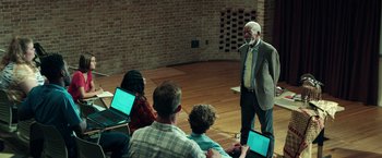 Movie still from “The Ritual Killer” (2023), directed by George Gallo – An older man standing in front of a group of young people; Wide shot, Over the shoulder angle