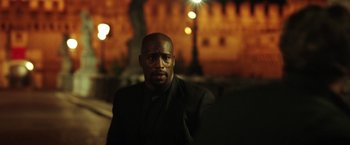 Movie still from “The Ritual Killer” (2023), directed by George Gallo – A man in a black jacket is standing in front of a building; Medium shot, Over the shoulder angle