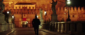 Movie still from “The Ritual Killer” (2023), directed by George Gallo – A man walking down a street at night past statues; Wide shot, Low angle