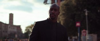 Movie still from “The Ritual Killer” (2023), directed by George Gallo – A man wearing a suit and tie standing in front of a building; Close Up shot, Low angle