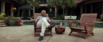 Movie still from “The Ritual Killer” (2023), directed by George Gallo – A man sitting in a chair on a patio next to a pool; Wide shot, Low angle