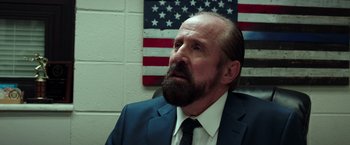 Movie still from “The Ritual Killer” (2023), directed by George Gallo – A man in a suit and a tie in front of an american flag; Close Up shot, Low angle