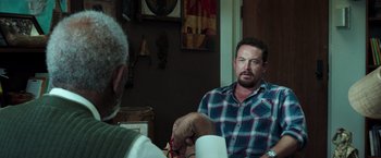 Movie still from “The Ritual Killer” (2023), directed by George Gallo – A man sitting in front of another man holding a pair of scissors; Medium shot, Over the shoulder angle