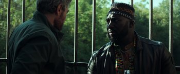 Movie still from “The Ritual Killer” (2023), directed by George Gallo – Two men are standing next to each other in front of a window; Close Up shot, Over the shoulder angle