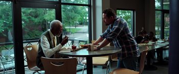Movie still from “The Ritual Killer” (2023), directed by George Gallo – Two men are sitting at a table and one of the men is holding a piece of pizza; Medium shot, Over the shoulder angle