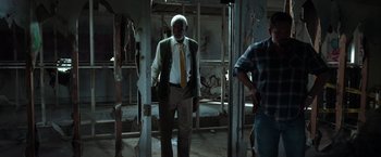 Movie still from “The Ritual Killer” (2023), directed by George Gallo – A man standing in a room with a man standing next to him; Medium shot, Low angle