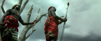 Movie still from “The Ritual Killer” (2023), directed by George Gallo – A man in a red and orange striped robe holding two spears; Medium shot, Low angle