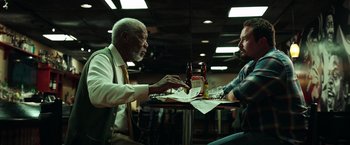 Movie still from “The Ritual Killer” (2023), directed by George Gallo – Two men are sitting at a table with beer bottles; Medium shot, Low angle