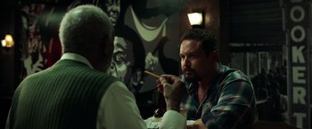 Movie still from “The Ritual Killer” (2023), directed by George Gallo – Two men are sitting at a table and one of them is holding chopsticks in his mouth; Close Up shot, Over the shoulder angle