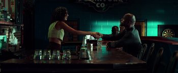 Movie still from “The Ritual Killer” (2023), directed by George Gallo – Two people shaking hands over a bar with drinks on the table; Medium shot, Low angle