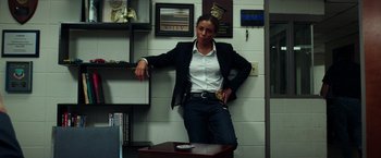 Movie still from “The Ritual Killer” (2023), directed by George Gallo – A woman leaning on a table in a room; Medium shot, Low angle