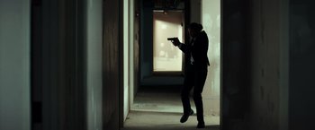 Movie still from “The Ritual Killer” (2023), directed by George Gallo – A person holding a gun in a room; Wide shot, Low angle