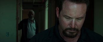 Movie still from “The Ritual Killer” (2023), directed by George Gallo – A man with a goatee and beard looking down; Close Up shot, Over the shoulder angle
