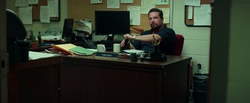 Movie still from “The Ritual Killer” (2023), directed by George Gallo – A man sitting at a desk in front of a computer; Medium shot, Low angle