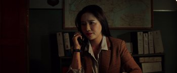 Movie still from “The Ritual Killer” (2023), directed by George Gallo – A woman talking on a phone while sitting at a desk; Close Up shot, High angle