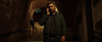 Movie still from “The Ritual Killer” (2023), directed by George Gallo – A man talking on a cell phone while wearing a jacket; Medium shot, Low angle