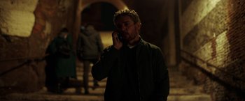 Movie still from “The Ritual Killer” (2023), directed by George Gallo – A man talking on a cell phone while standing in a dark room; Medium shot, Low angle