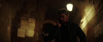 Movie still from “The Ritual Killer” (2023), directed by George Gallo – A man talking on a cell phone while standing in a dark room; Close Up shot, Low angle