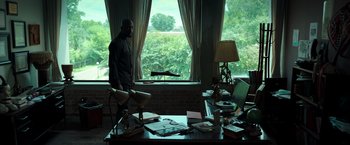 Movie still from “The Ritual Killer” (2023), directed by George Gallo – A man standing in front of a desk in front of a window; Wide shot, Low angle
